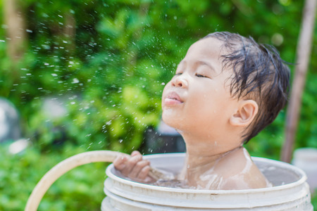 Blurred photo of children play and bathed water in the garden,sitting in a bucket of water. Concept of raising childrenの写真素材