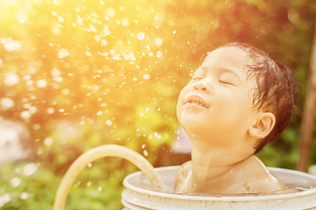 Blurred photo of children play and bathed water in the garden,sitting in a bucket of water. Concept of raising children.の写真素材