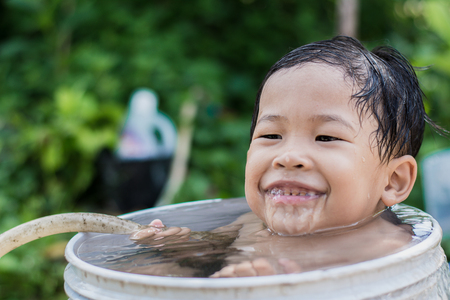 Children play and bathed water in the garden,sitting in a bucket of water. Concept of raising children.の写真素材