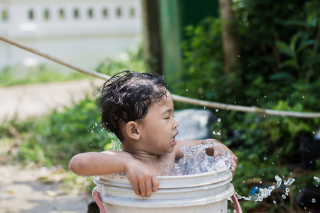 Children play and bathed water in the garden,sitting in a bucket of water. Concept of raising children.の写真素材