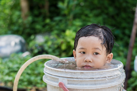 Children play and bathed water in the garden,sitting in a bucket of water. Concept of raising children.の写真素材