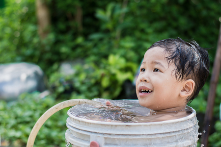 Children play and bathed water in the garden,sitting in a bucket of water. Concept of raising children.の写真素材
