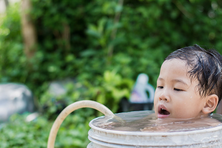 Children play and bathed water in the garden,sitting in a bucket of water. Concept of raising children.の写真素材