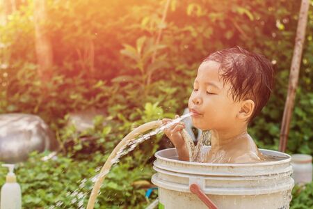 Children play and bathed water in the garden,sitting in a bucket of water. Concept of raising children.の写真素材