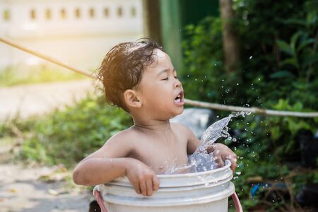 Children play and bathed water in the garden,sitting in a bucket of water. Concept of raising children.の写真素材