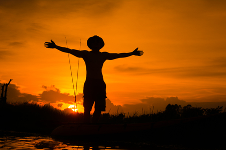 Silhouette traveler man relaxing on the beach with fishing rod and raise hand him arms open felling freedom.の写真素材