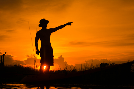 Silhouette of fisherman on the boat pointing with finger in sky.の写真素材