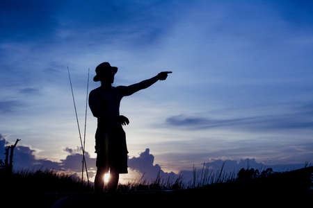 Silhouette of fisherman on the boat pointing with finger in sky.の写真素材