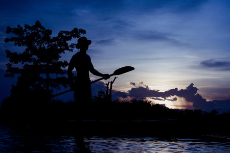 Silhouette of  fisherman standing on boat,hold paddle,on sunset background.の写真素材
