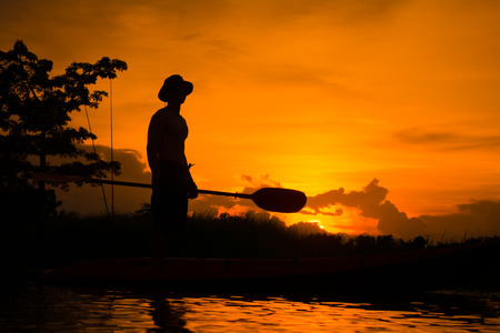 Silhouette of  fisherman standing on boat,hold paddle,on sunset background.の写真素材