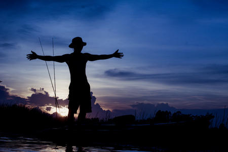 Silhouette traveler man relaxing on the beach with fishing rod and raise hand him arms open felling freedom.の写真素材