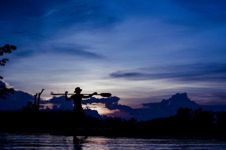Silhouette of  fisherman standing on boat,hold paddle,on sunset background.の写真素材