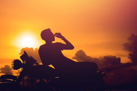 Silhouette of man and a motorcycle with sunset background.の写真素材