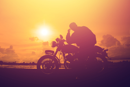 Silhouette of man and a motorcycle with sunset background.の写真素材