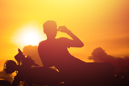 Silhouette of man and a motorcycle with sunset background.の写真素材