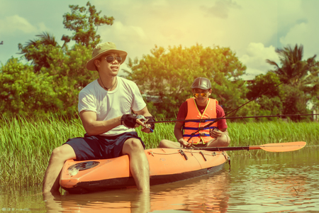 Young man and brother fishing during in The River, He sitting on his boat. Man Relaxing During Vacation.の写真素材