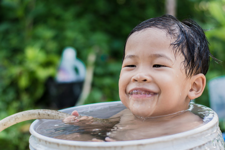 Children play and bathed water in the garden,sitting in a bucket of water. Concept of raising children.の写真素材