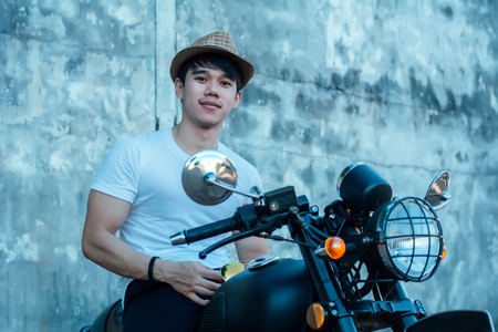 Handsome young men with black color classic motobike(motorcycle) on cement background.の写真素材