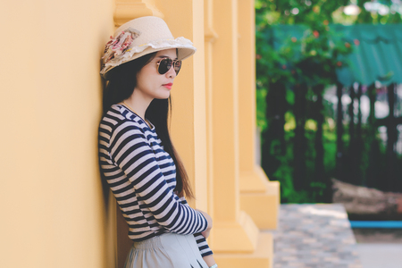 Close up shot of stylish young woman in sunglasses and hat against Yellow building background. Beautiful female model with copy space.の写真素材