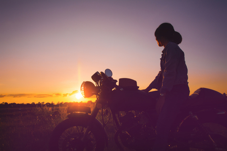 Silhouette of young woman drive with motorcycle on street, enjoying freedom and active lifestyle, having fun on a bikers tour on sunset background.の写真素材