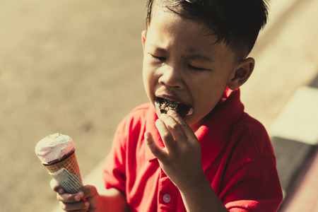 Kid eating ice cream in waffles cone and winking on park outdoor background.の写真素材