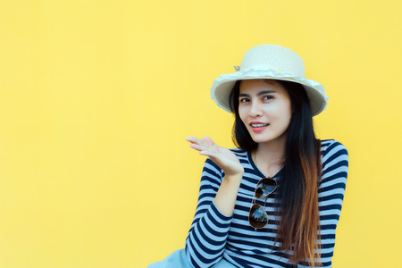 Sunny lifestyle fashion portrait of young stylish hipster woman beside building against yellow background, wearing trendy outfit, hat, travel concept.の写真素材