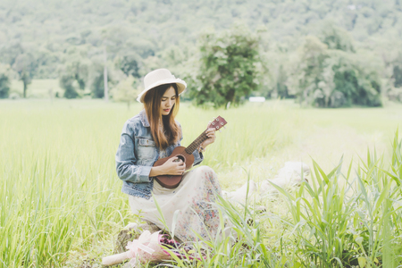 Young woman in a field , rounded sunglasses and straw hat and ukulele having fun outdoor in countryside.Awesome warm summer day.の写真素材