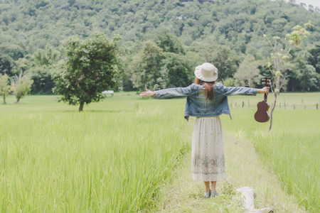 Young woman in a field , rounded sunglasses and straw hat and ukulele having fun outdoor in countryside.Awesome warm summer day.の写真素材