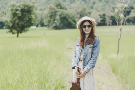 Young woman in a field , rounded sunglasses and straw hat and ukulele having fun outdoor in countryside.Awesome warm summer day.の写真素材