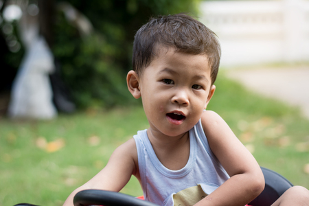 Little boy driving car with the steering wheel. Boy in a white shirt in a red toy car in the street. Little boy driving big toy car and having fun, outdoors.の写真素材