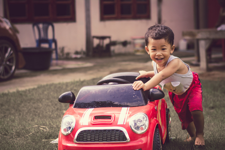 Little boy driving red car with the steering wheel. Little boy driving big toy car and having fun on grass outdoors.の写真素材