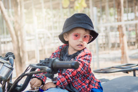 Close up of a boy wearing  hat and fashion glasses.He riding a quad bike on the farm is in a good mood.の写真素材