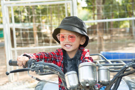 Close up of a boy wearing  hat and fashion glasses.He riding a quad bike on the farm is in a good mood.の写真素材