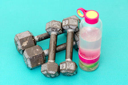 Old and very much used gym and training iron dumbbells or exercise weights and a juice bottle on a turquoise matの写真素材