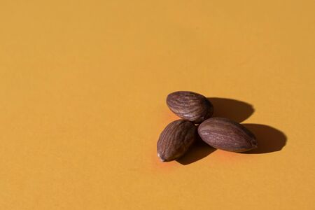 a bunch of three almonds in the lower right corner on an orange background; studio light still lifeの写真素材