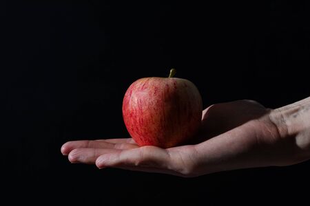 red apple in hand on a black background; studio photoの写真素材