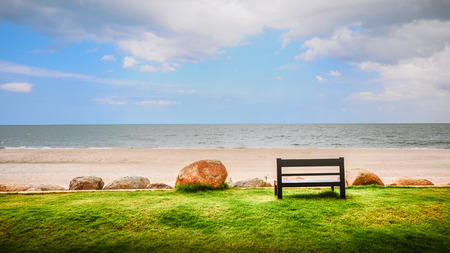 A Wooden Bench Near a White Sand Beach Looking to the Oceanの写真素材