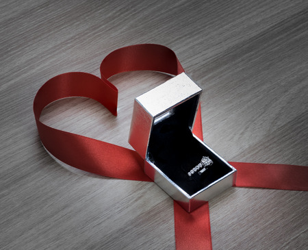 Wedding ring and red heart ribbon on wooden surface for valentines or marriage proposalの写真素材