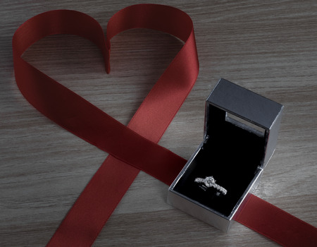 Wedding ring and red heart ribbon on wooden surface for valentines or marriage proposalの写真素材