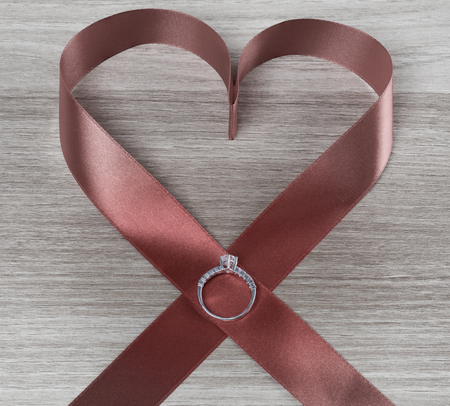 Wedding ring and red heart ribbon on wooden surface for valentines or marriage proposalの写真素材