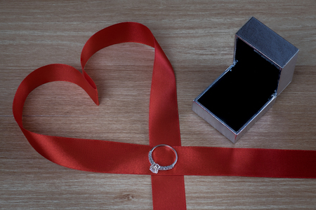 Wedding ring and red heart ribbon on wooden surface for valentines or marriage proposalの写真素材