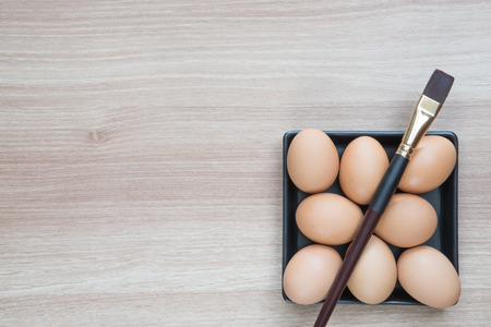 Eight eggs in black square plate with a brush on wooden surface ready for Easter painting with space for textの写真素材
