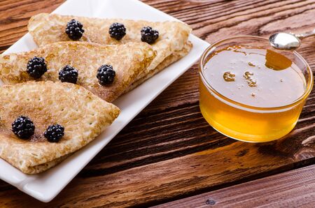 pancakes with honey and blackberries on a wooden tableの写真素材