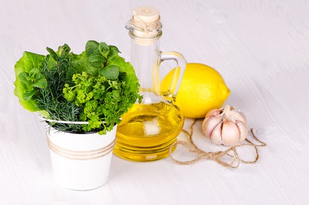 Fresh herbs in a bucket with lemon and olive oil on a light woodの写真素材