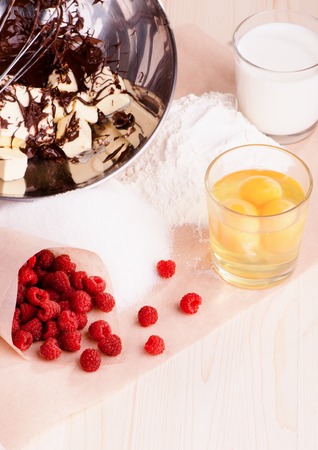 ingredients for baking, raspberries, sugar, flour, eggs, chocolate, butter, cream lay on parchmentの写真素材