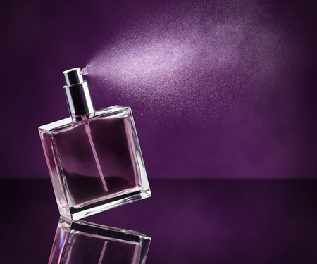 perfume bottle spraying on dark purple backgroundの写真素材