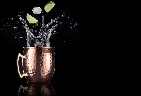 lime and ice falling into a splashing moscow mule cocktail isolated on black backgroundの写真素材