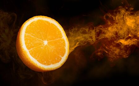 close up of a cut orange in a smoke swirl flying on dark backgroundの写真素材