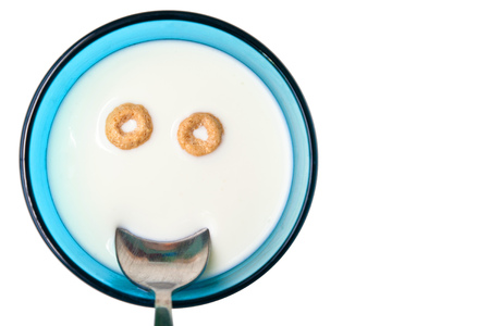 Pieces of a dry breakfast in the form of a happy smile in a bright blue cup with a spoon isolatedの写真素材