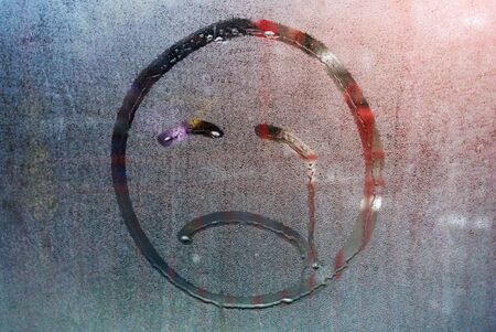 Wet home window with raindrops. Trees behind a wet window. Sad smiley of raindropsの写真素材